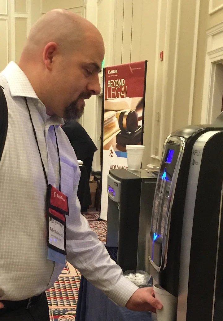 A man filling a paper cup with water from a water dispenser at a conference event.