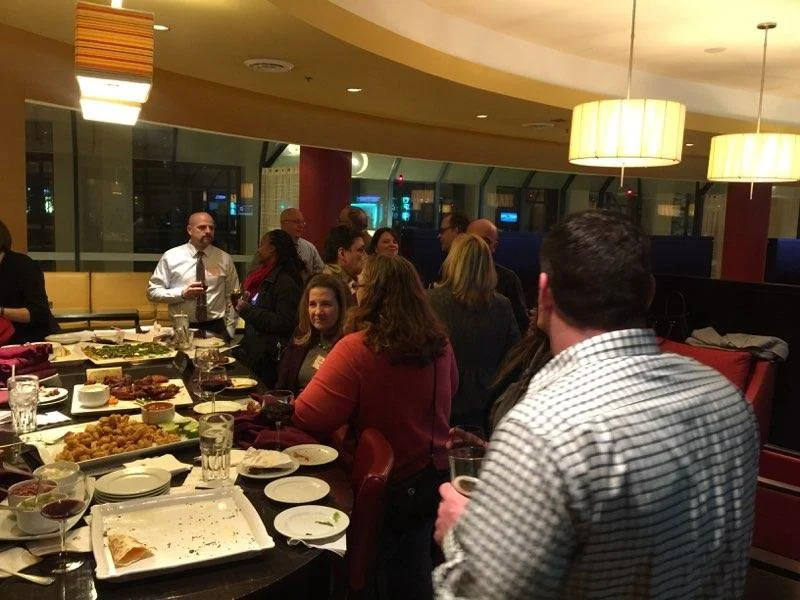 People socializing around a dining table with food and drinks in a restaurant or banquet setting.