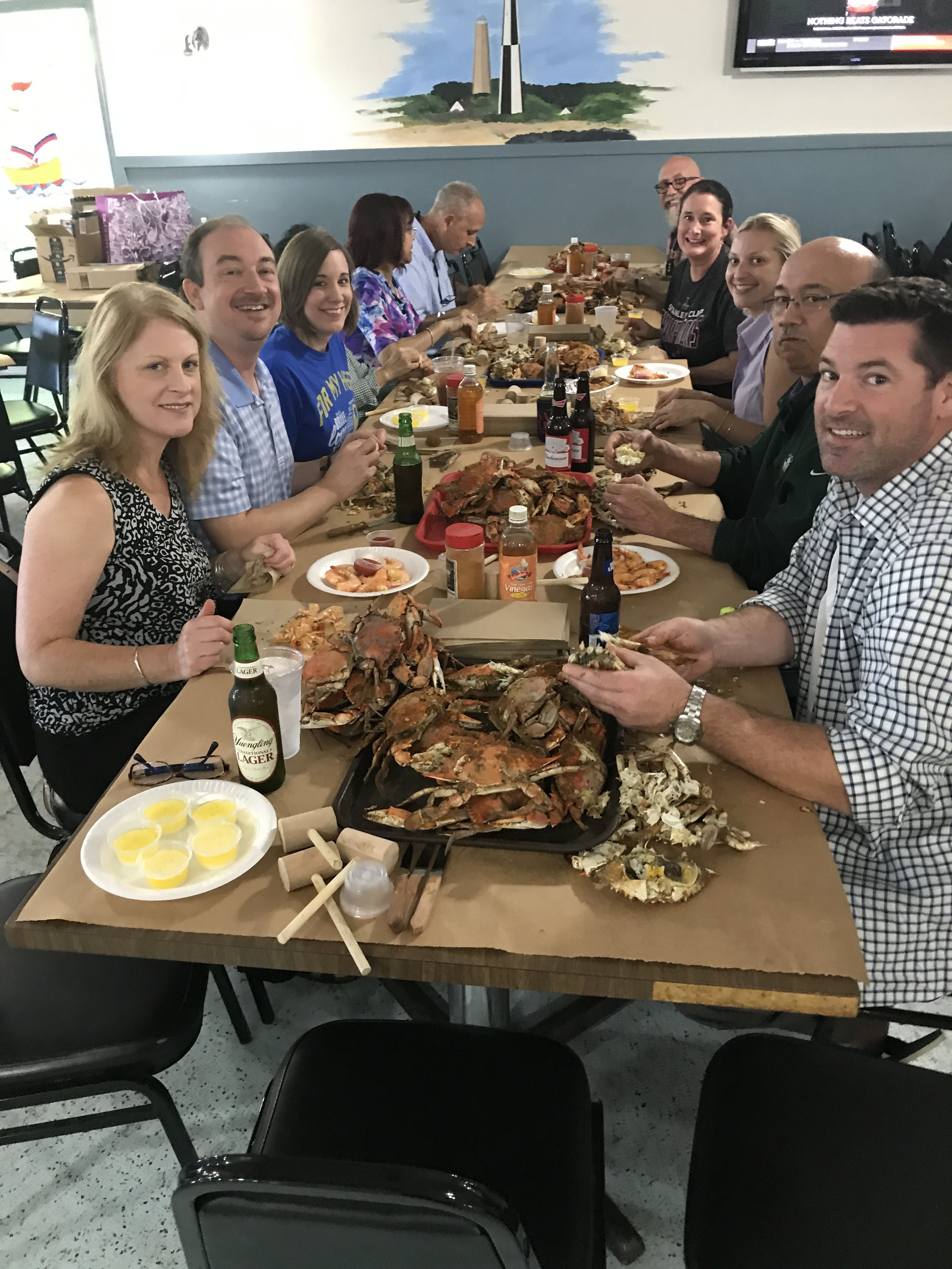 People gathered around a table enjoying a seafood feast with cooked lobsters, shrimp, and various sauces in a restaurant setting.