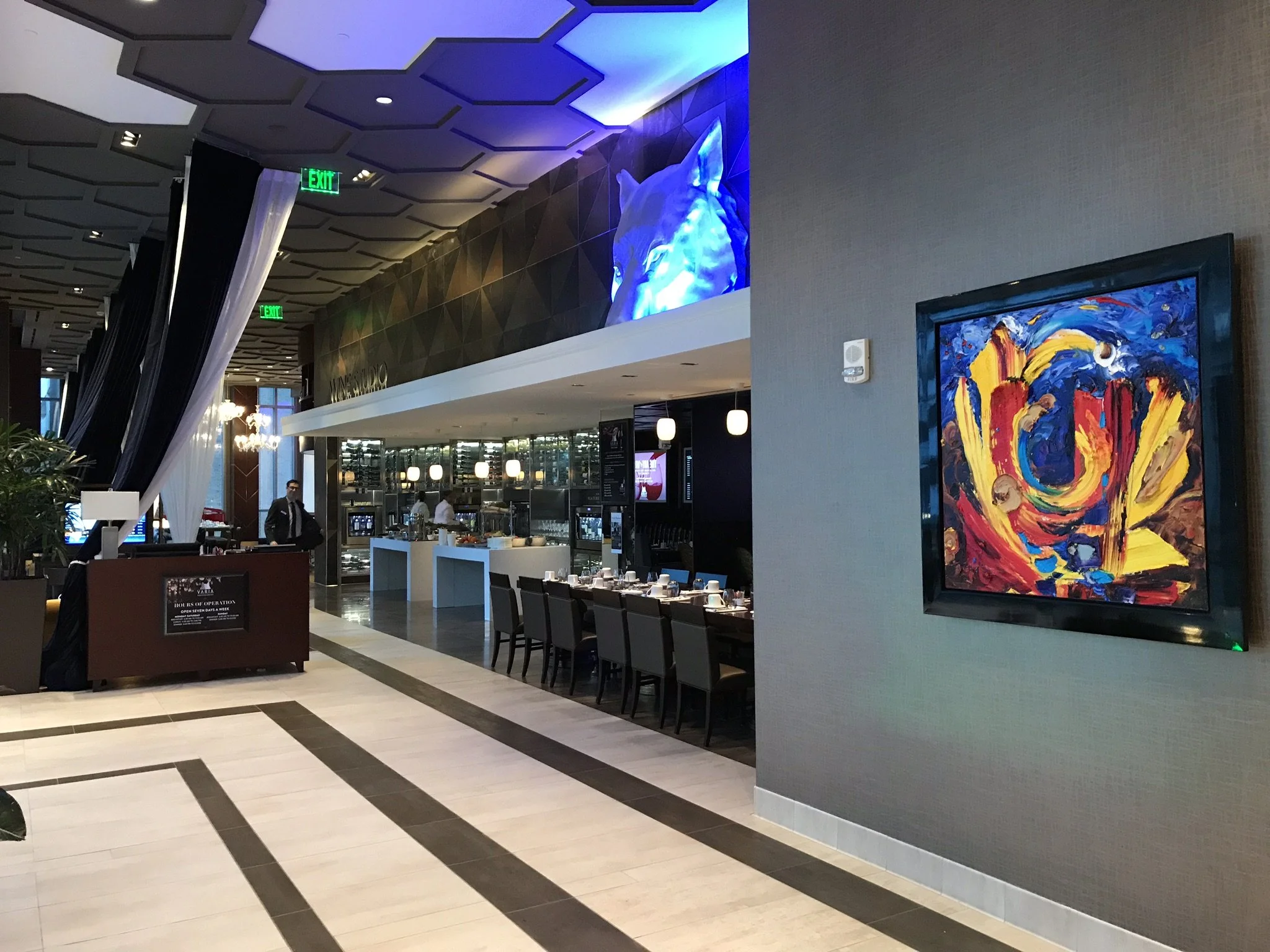 Interior of a modern restaurant or hotel lobby with artwork, seating, and a café counter in the background.