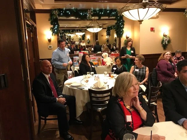 People seated around a decorated banquet table at a holiday party in a warmly lit restaurant with Christmas decorations and a mirrored wall.