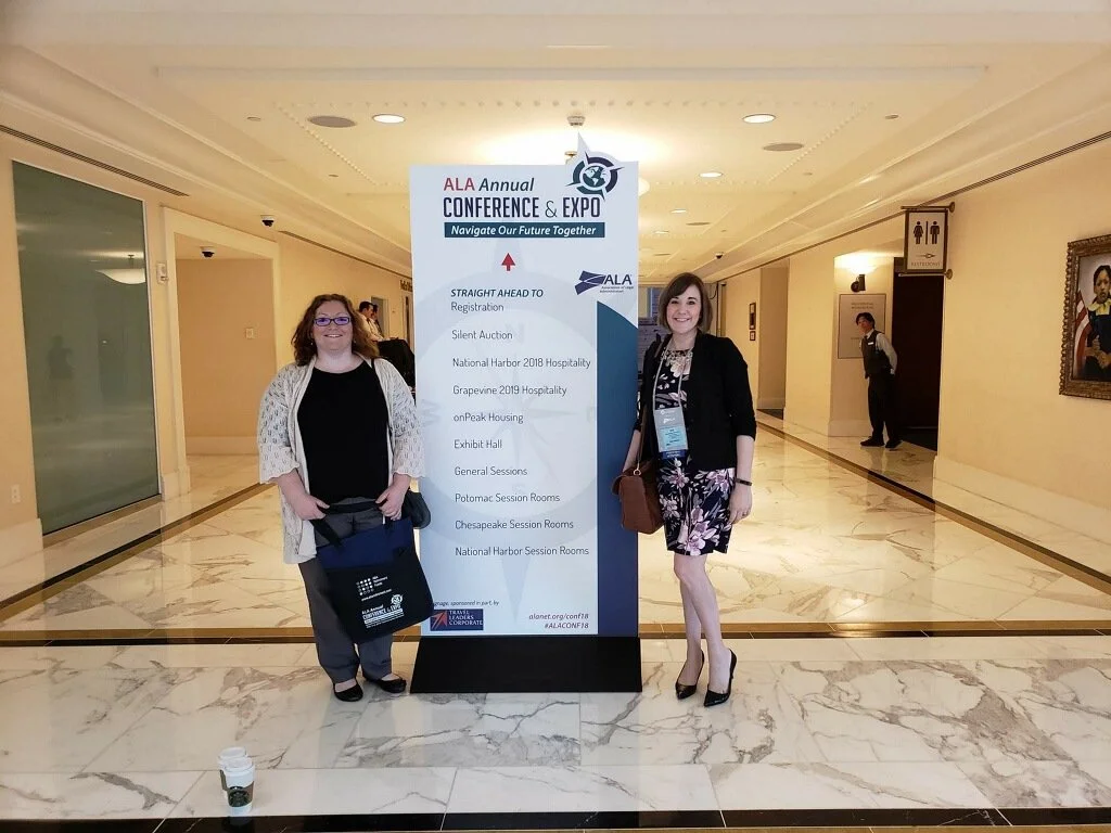 Two women standing in front of a conference sign at the ALA Annual Conference & Expo, smiling for the photo.