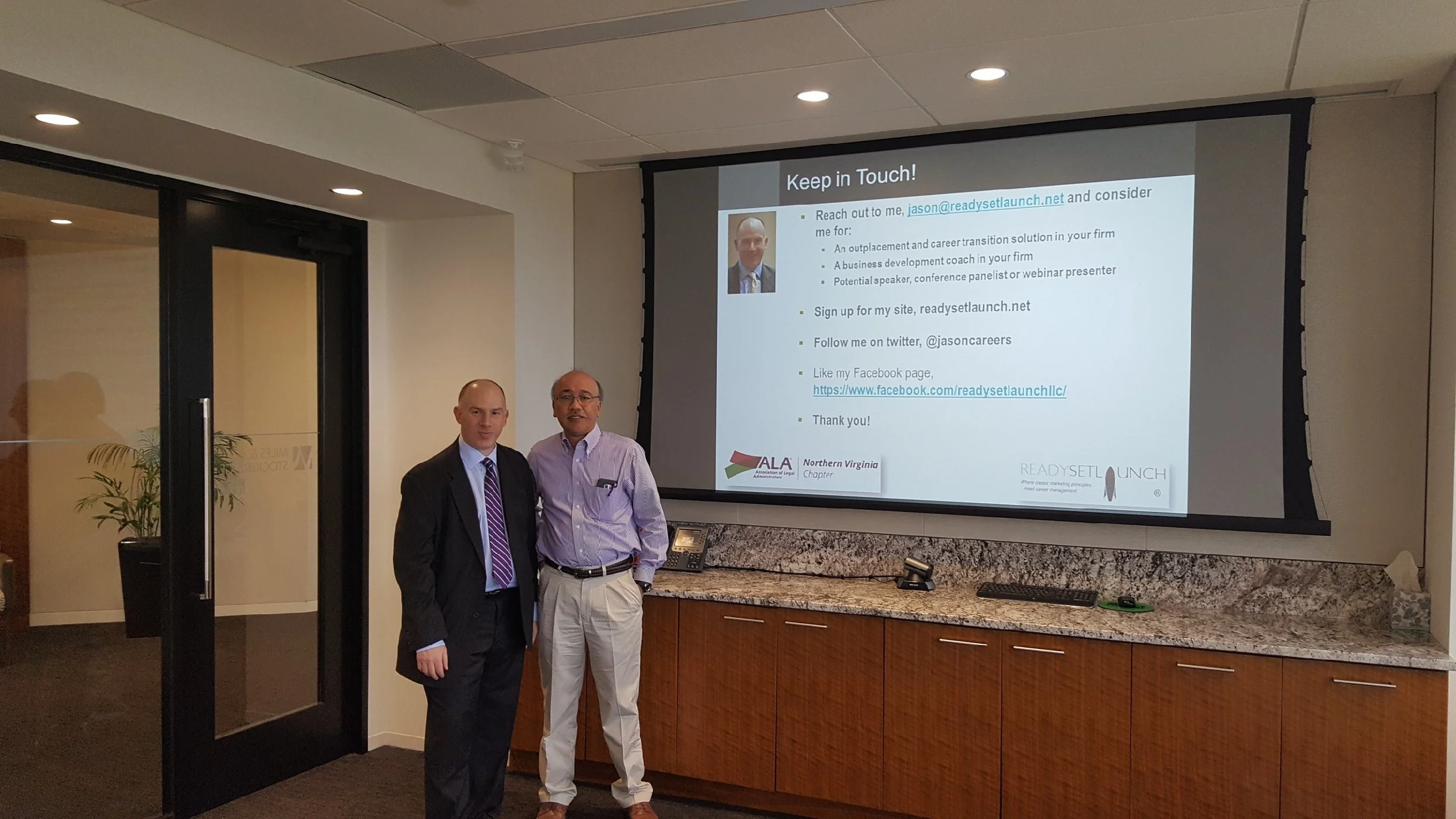 Two men standing in front of a presentation screen at a conference or meeting. The screen displays contact information and details for a professional networking or mentorship opportunity, with a logo of the Northern Virginia Chapter of the American L