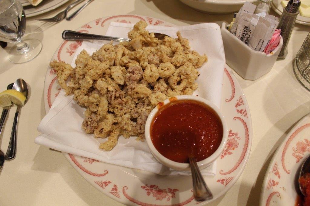 Fried calamari with a side of marinara sauce served on a decorative plate at a restaurant.