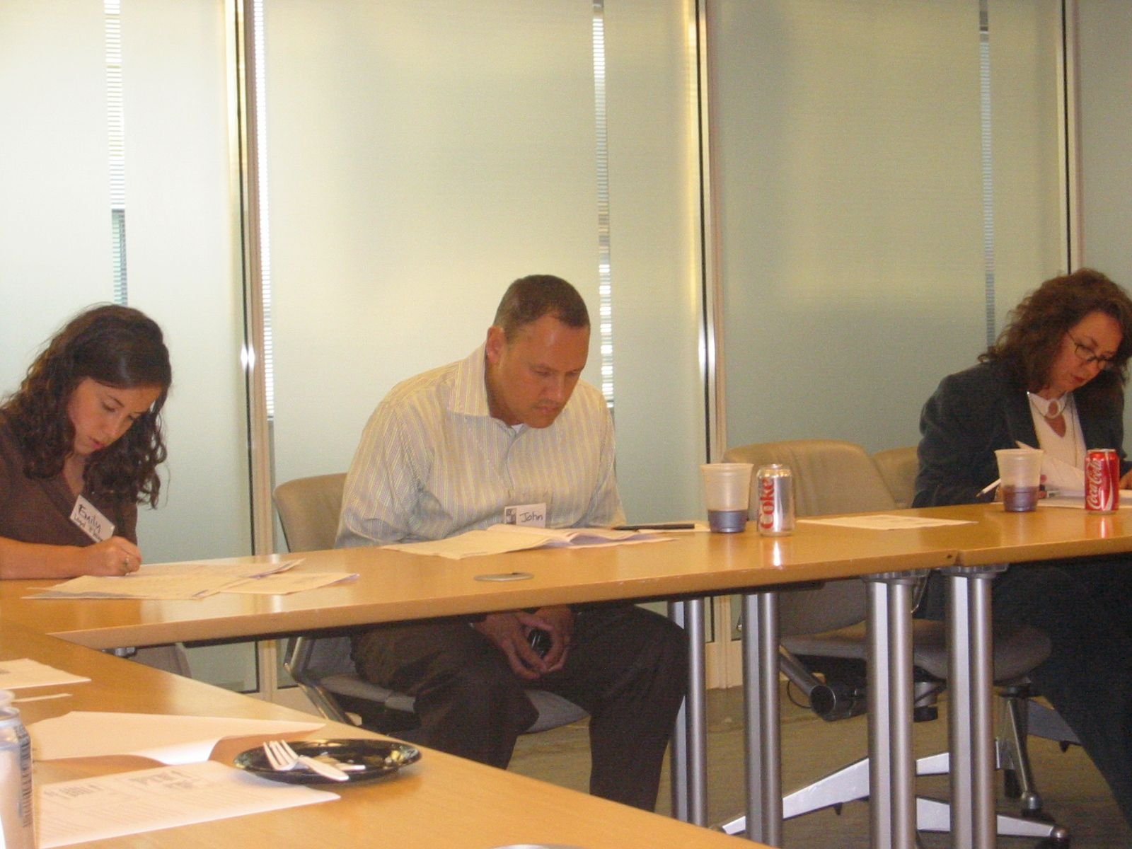 Three people sitting at a conference table, reading documents, with drinks and snacks on the table.