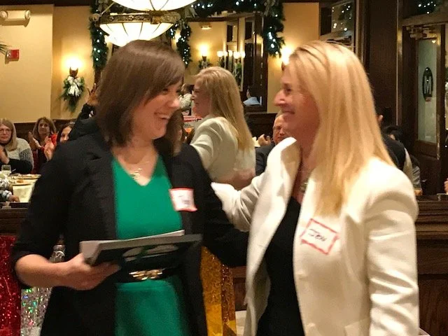 Two women talking and smiling at a social event in a decorated restaurant or banquet hall.