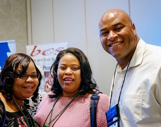 Three smiling people, two women and one man, at a professional event or conference.
