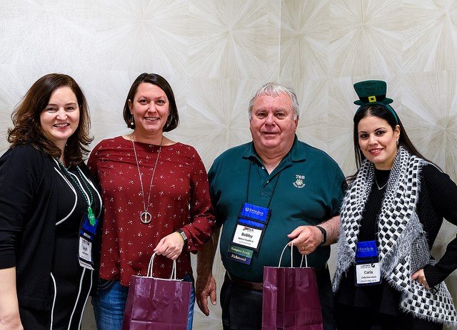 Four people standing together at an event, smiling, with name tags and gift bags.