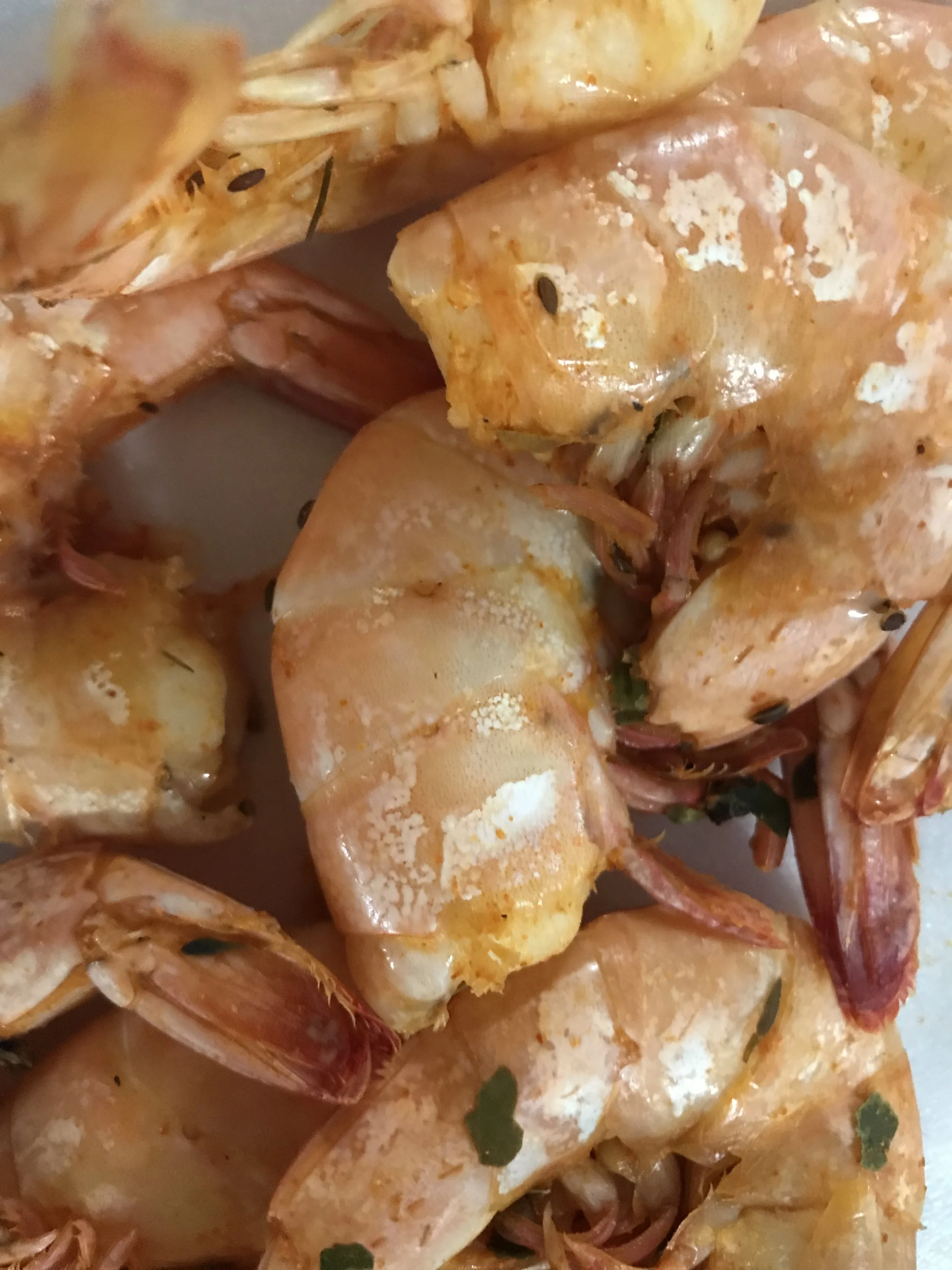 Close-up of cooked shrimp with shells and seasoning garnished with herbs.