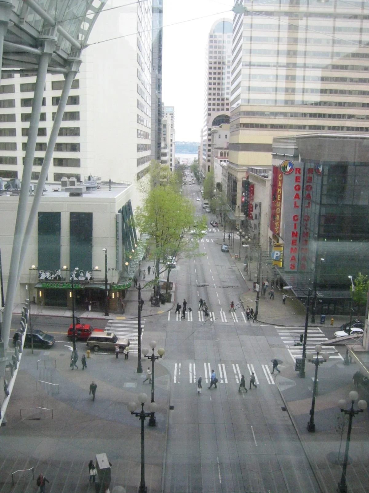 View of a city street from a tall building, with pedestrians walking across crosswalks, surrounded by large office buildings and a sign for a Regal Cinemas movie theater.