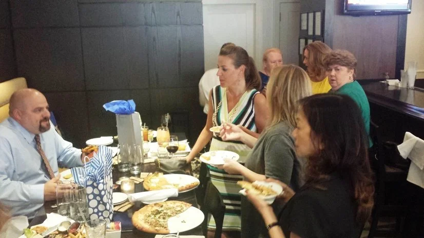 People gather around a table in a restaurant, enjoying pizza and drinks.