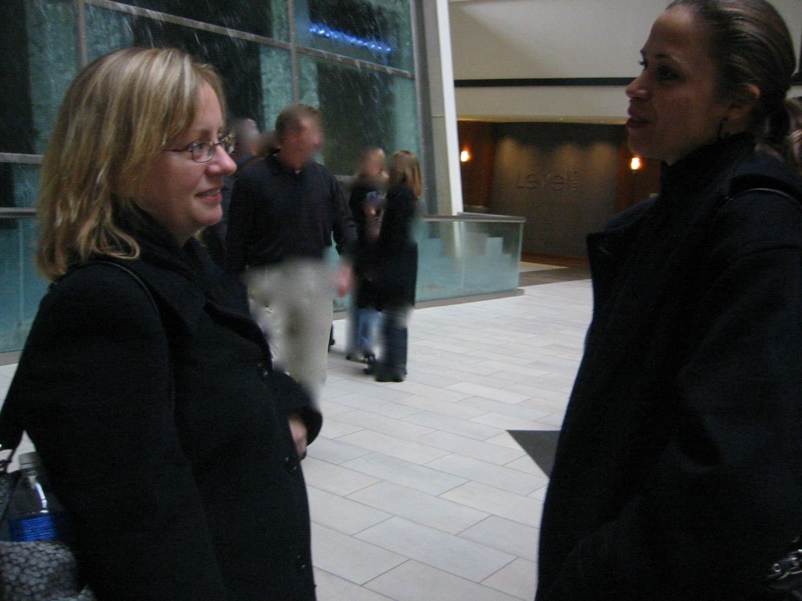 Two women standing face-to-face and engaged in conversation in an indoor public space.