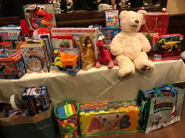 Table filled with various toys including stuffed animals, electronics, games, and gift bags.