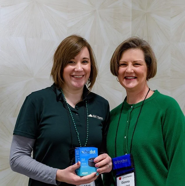 Two women smiling and standing close together indoors, one holding an Amazon Echo Dot box, and wearing a name tag that says Donna.