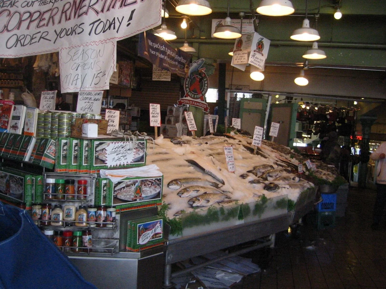 Display of fresh fish and seafood on ice at a market, with signs and packaging in the background.