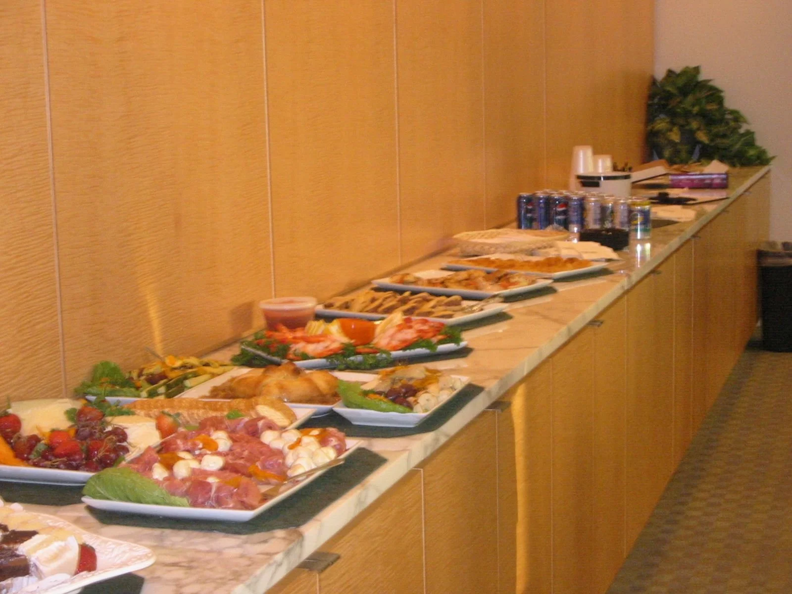 Buffet table with various dishes and canned drinks in a room with wood-paneled walls.