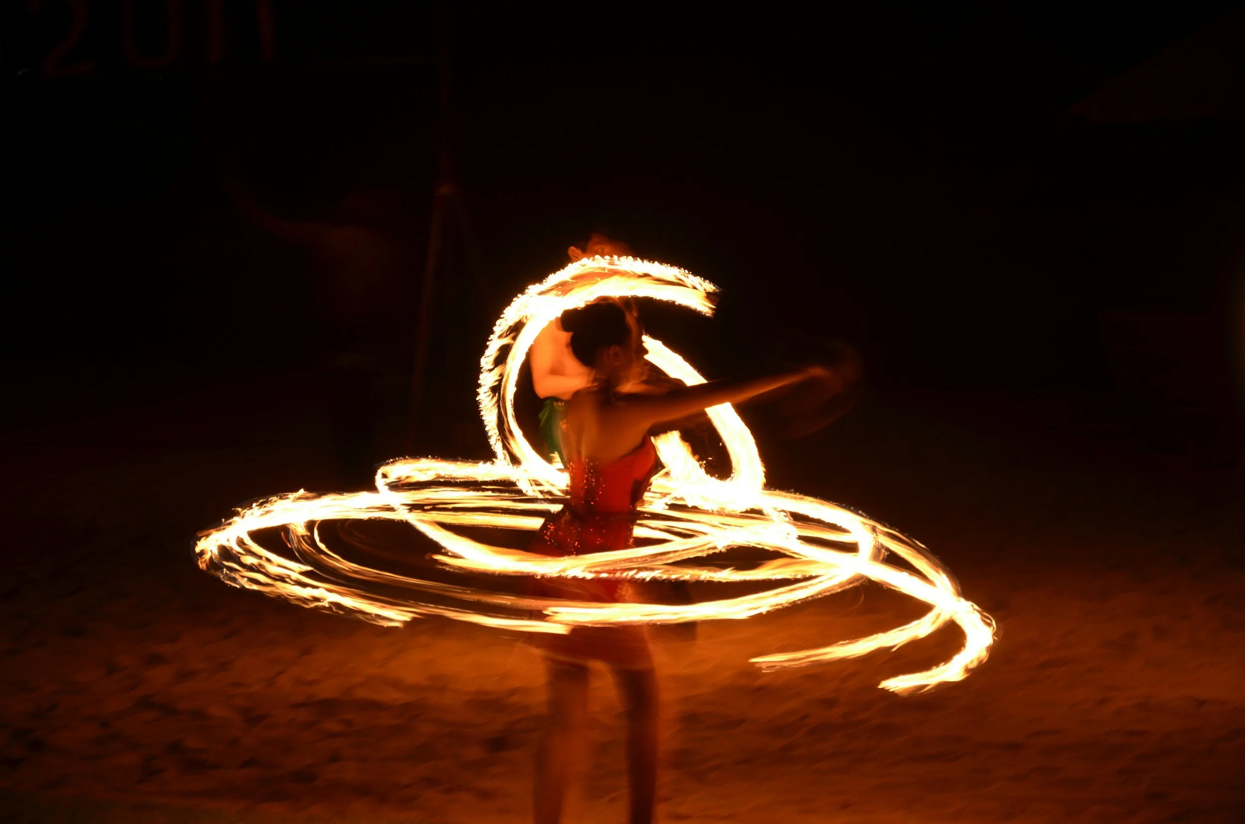 A performer spinning fire in the dark, creating circular trails of flames around their body.