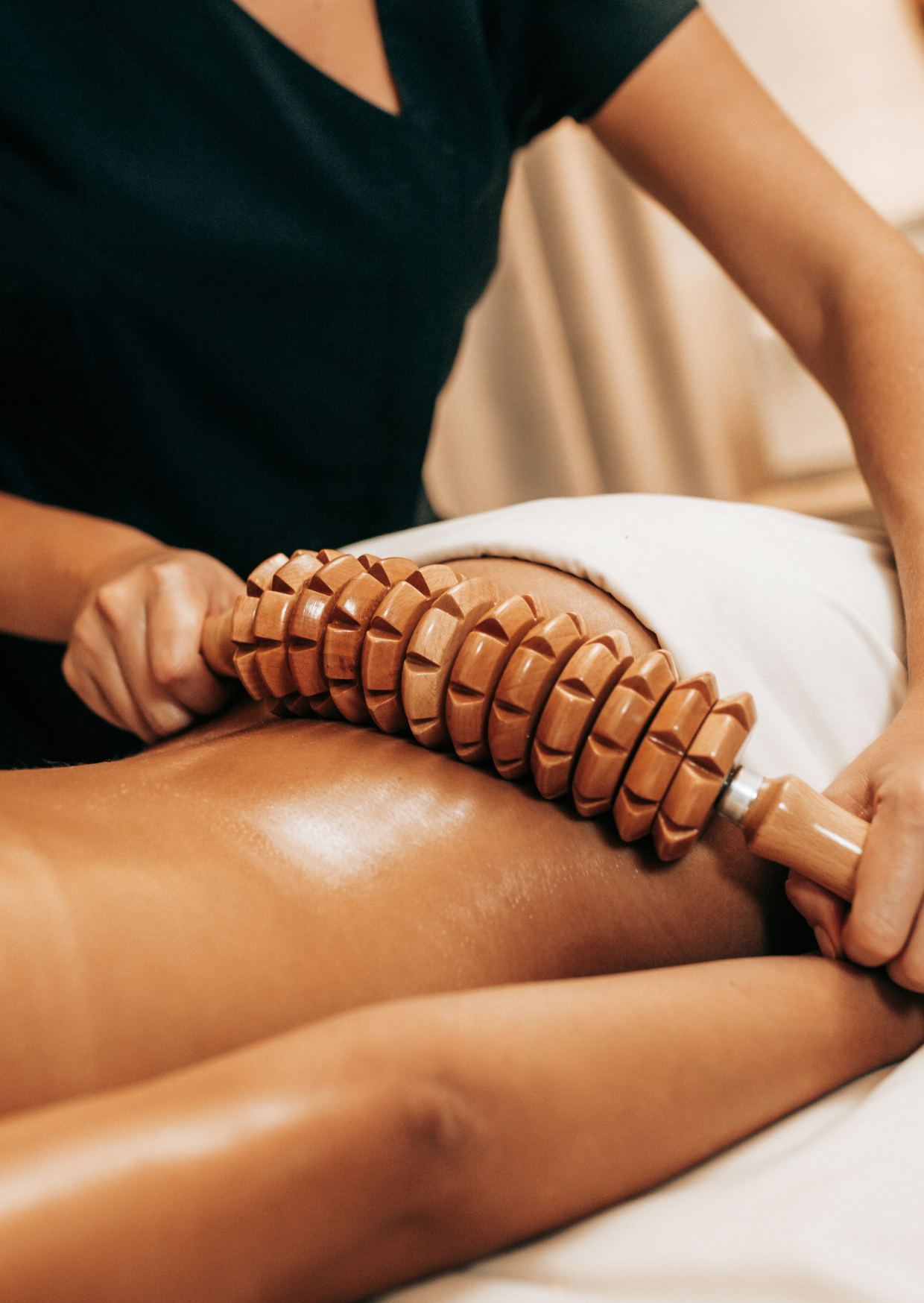 Una persona recibiendo un tratamiento de terapia de masaje con un rodillo de madera en el lombo, en un ambiente de spa o centro de bienestar.