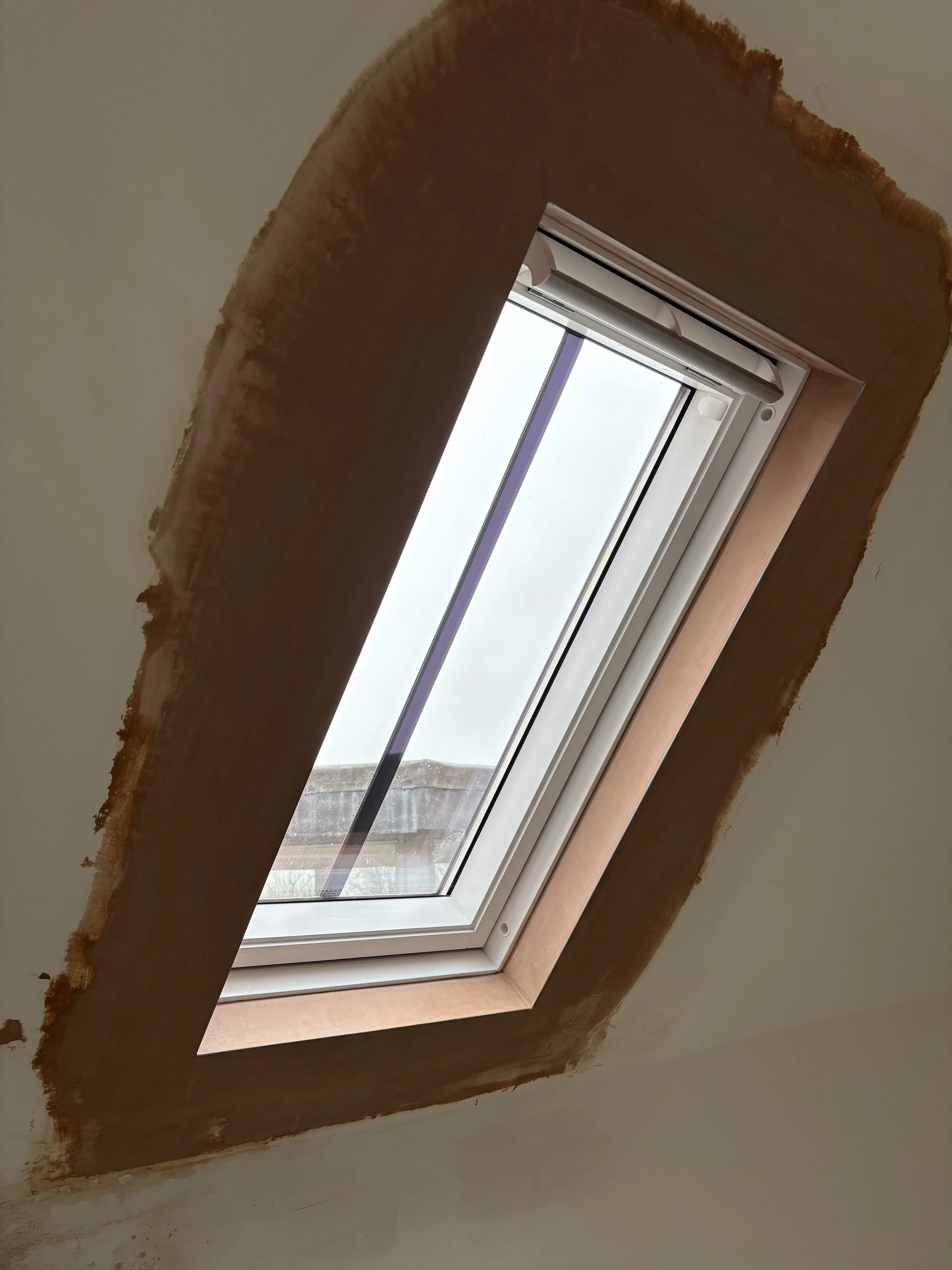 A skylight window installed in a ceiling with a view of the sky and partly cloudy weather outside.