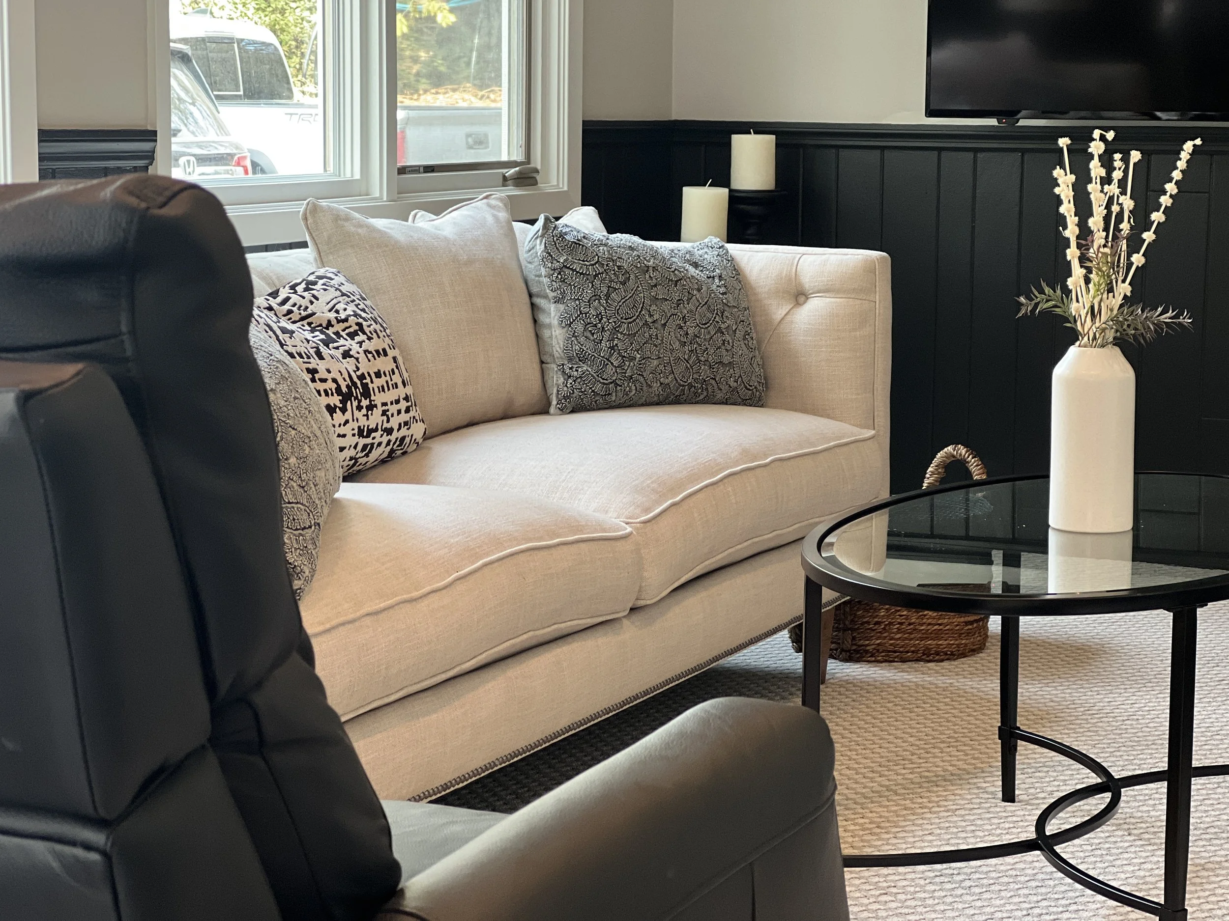 A modern living room with a tan couch and glass center table with beige carpet