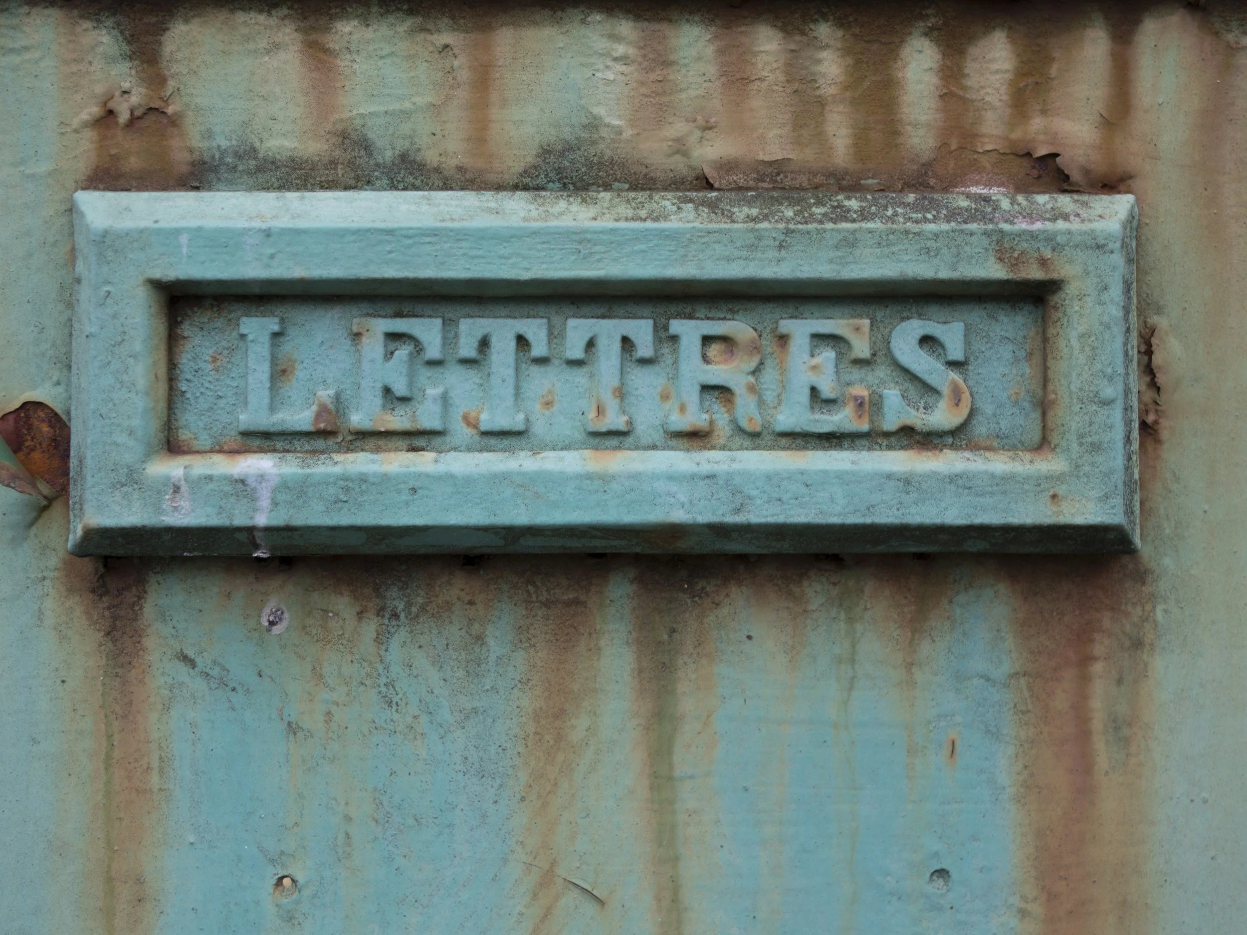 Close-up of an aged, weathered metal surface with peeling paint and a faded, embossed 'LETTERS' sign.