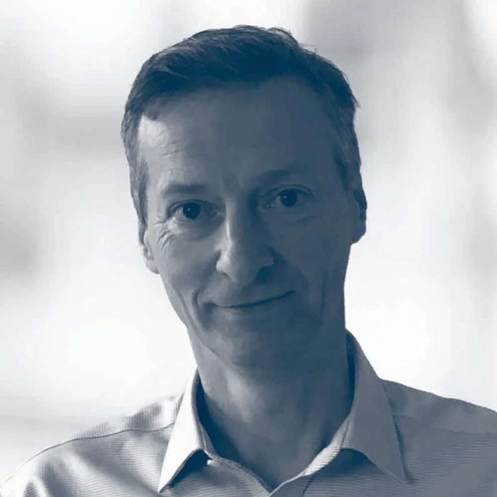 A man with short dark hair and a light shirt smiling at the camera in a grayscale photo.