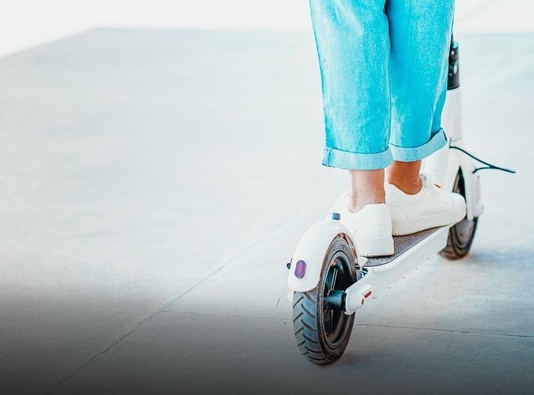 Person in blue jeans and white sneakers riding a white electric scooter on a concrete surface.