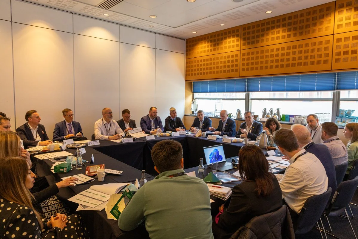 A group of business professionals seated around a conference table in a meeting room, engaging in a discussion.