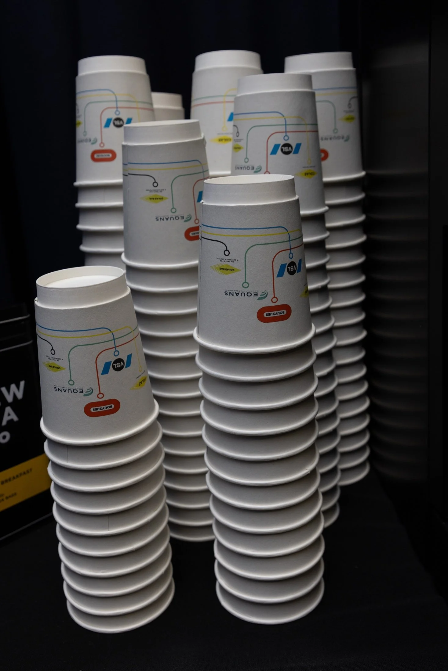 Stacked paper cups with a Transit Authority logo and colorful transit map design, arranged on a black surface.