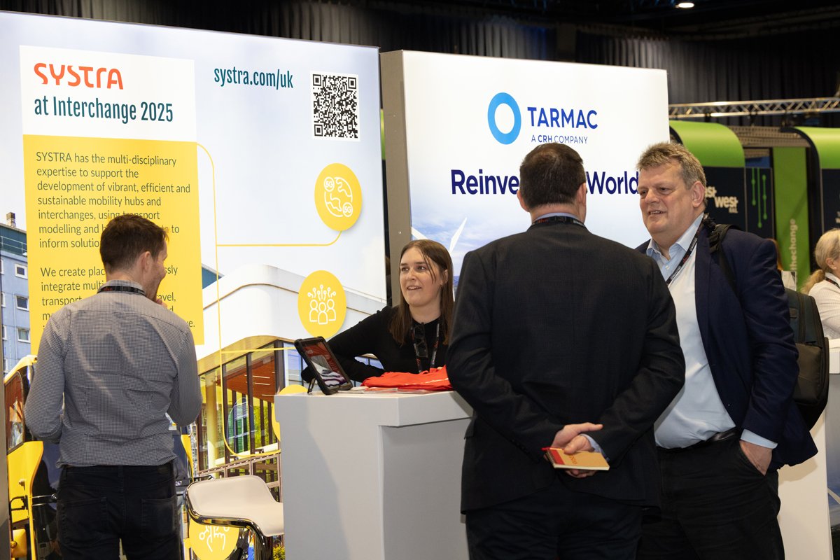 People engaging in conversation at a trade show booth with banners for SYSTRA and TARMAC in the background.