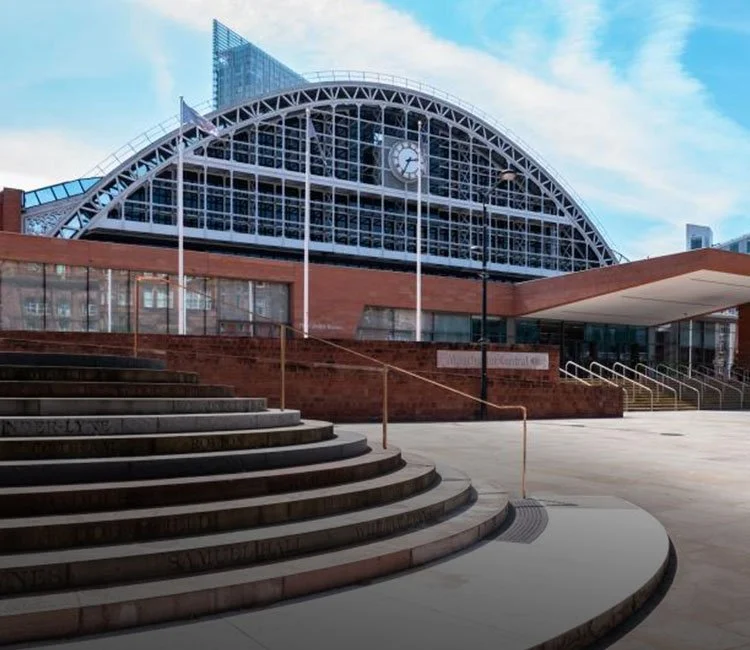 Modern train station with a large arched glass roof, a clock on the facade, and concrete stairs leading up to the entrance.