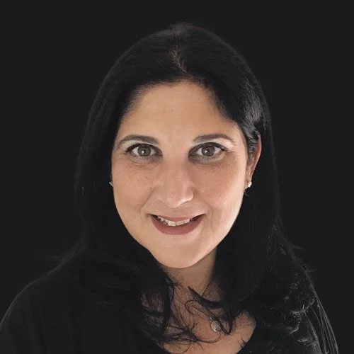 A woman with long black hair smiling against a black background.