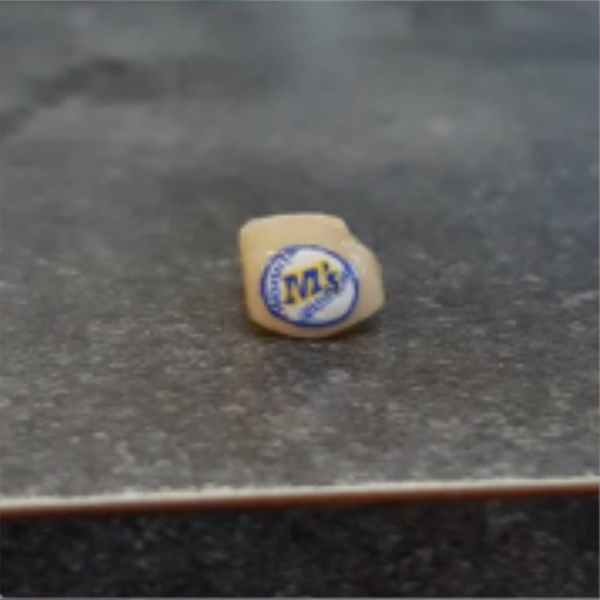 A small yellow candy with a blue and yellow logo sitting on a gray surface.