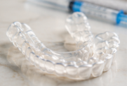 A clear dental night guard on a light-colored surface with a syringe in the background.