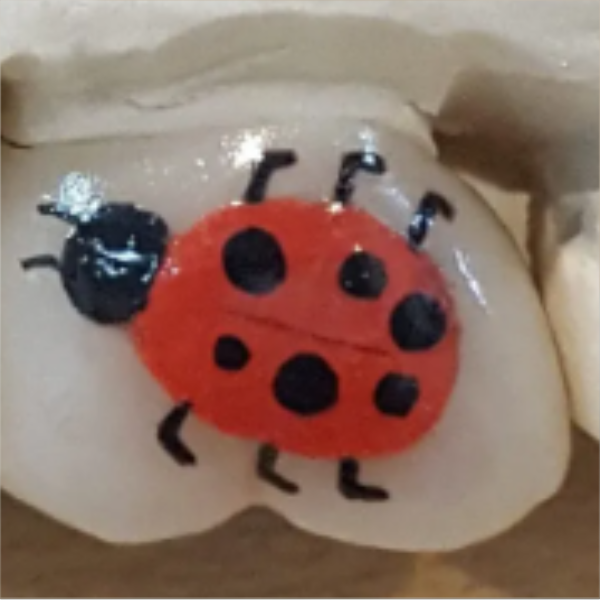 A painted ladybug with black spots on its red body, black head, antennae, and legs on a beige surface.