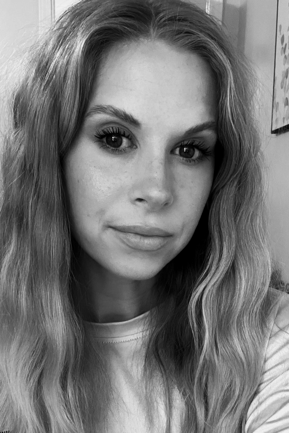 A woman with long wavy hair and clear skin looking at the camera in a grayscale photo.