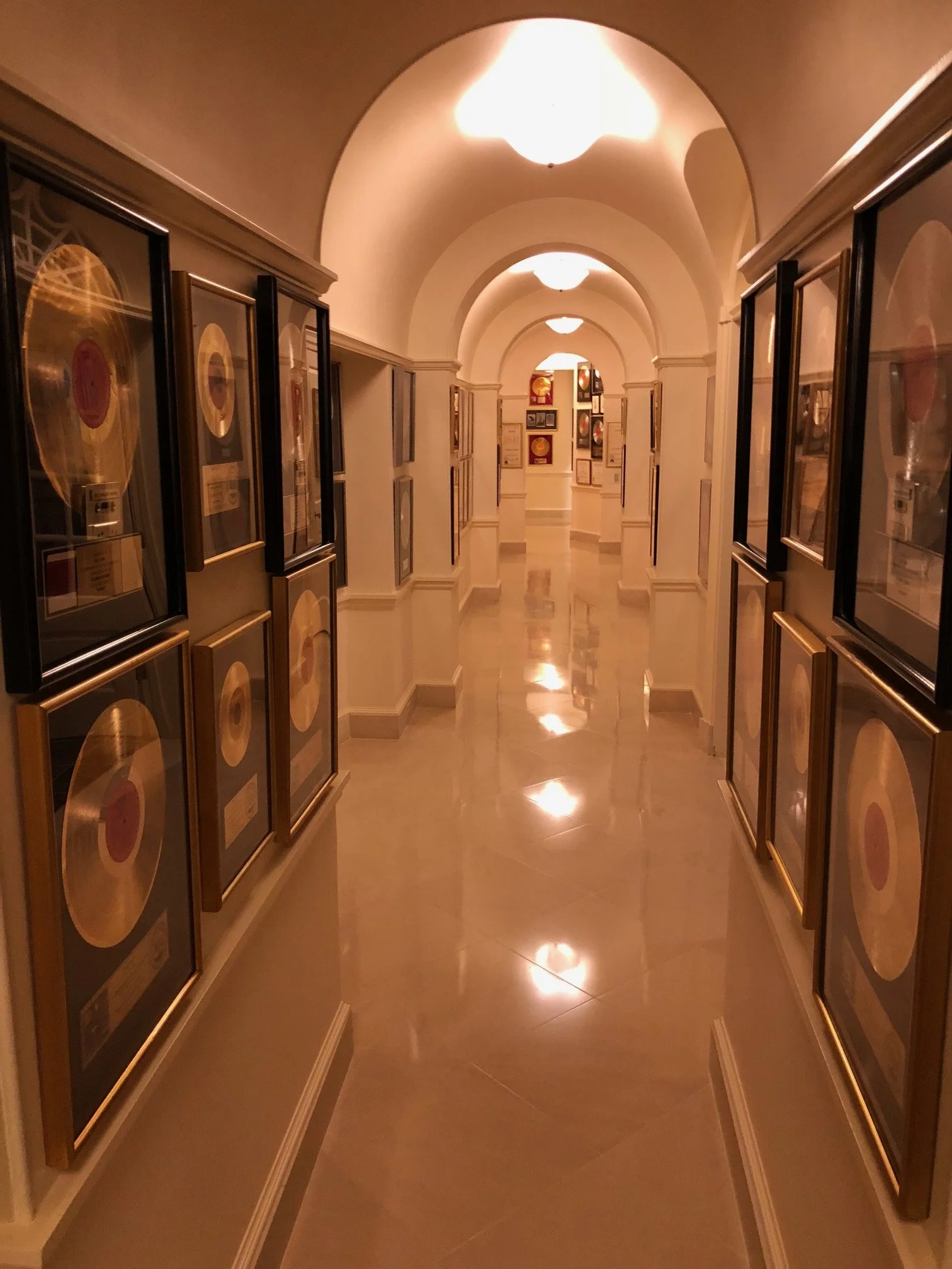 A hallway in a music awards museum displaying framed gold records on both sides with a polished floor and arched ceiling lights.