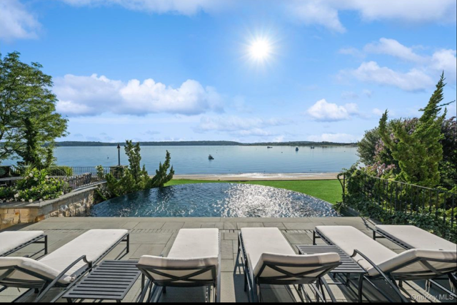 Pool area overlooking a lake with lounge chairs and greenery under a sunny sky.