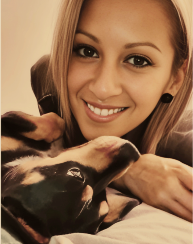 Lilly smiling and lying next to her dog Jaeda on the bed.