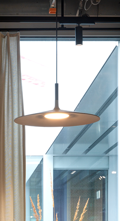 Modern hanging ceiling lamp in a room with large windows and a glass wall, white curtains, and daylight outside.