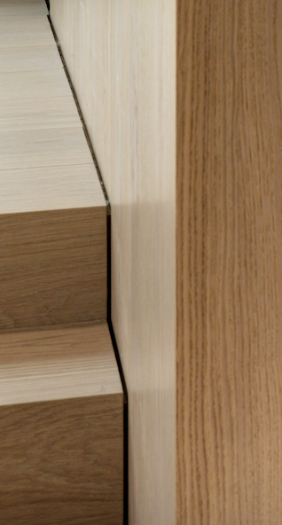 Close-up of a staircase corner with wooden steps, beige wall, and wooden paneling.