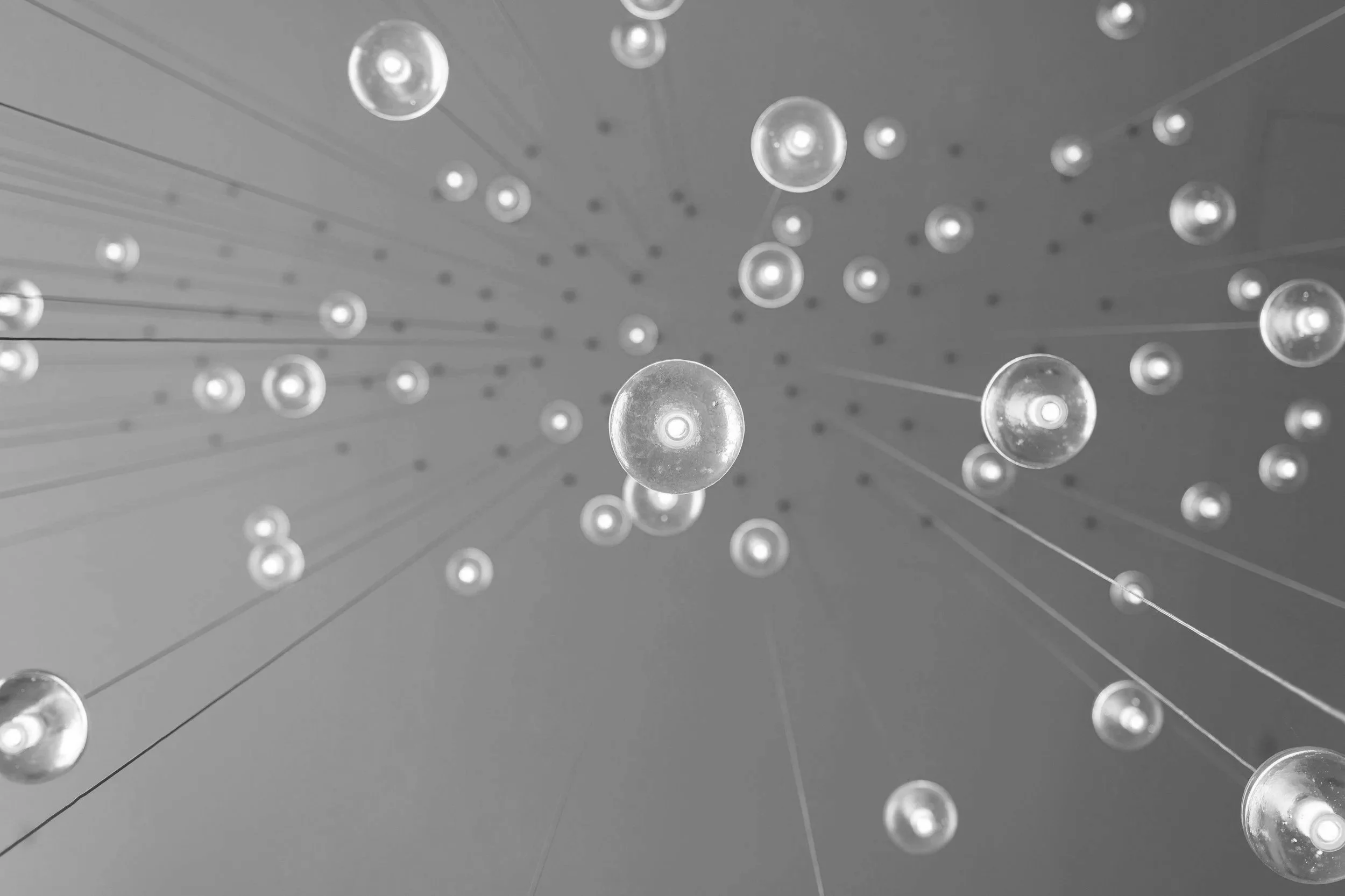 A modern chandelier with multiple spherical glass bulbs suspended from thin wires against a ceiling.