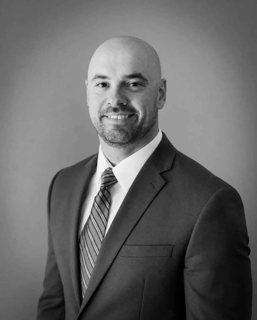 Black and white professional headshot of a bald man in a suit, smiling, against a plain background.