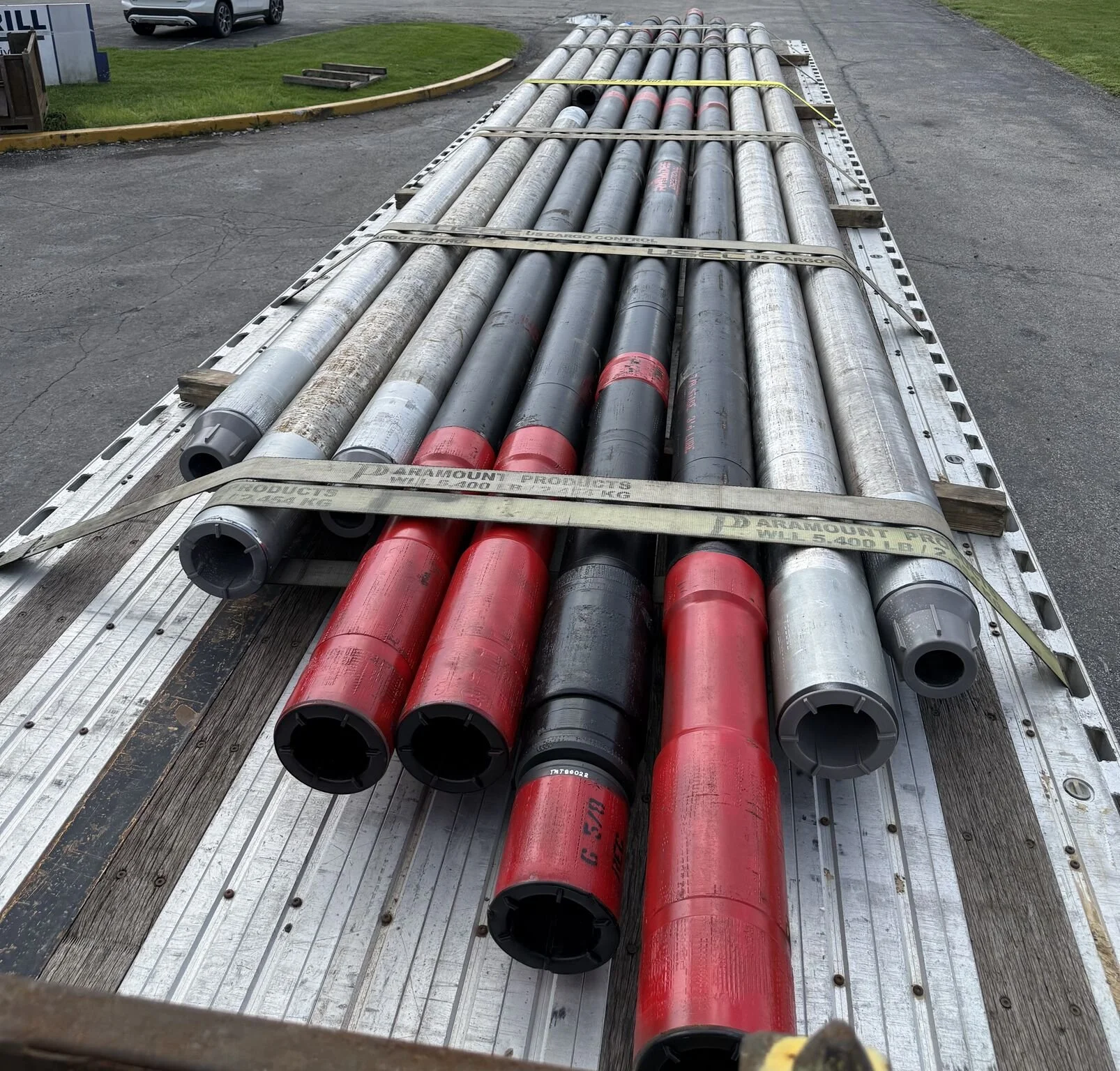 A flatbed truck carrying multiple black and red drilling motors stacked in parallel on wooden supports and secured with straps.