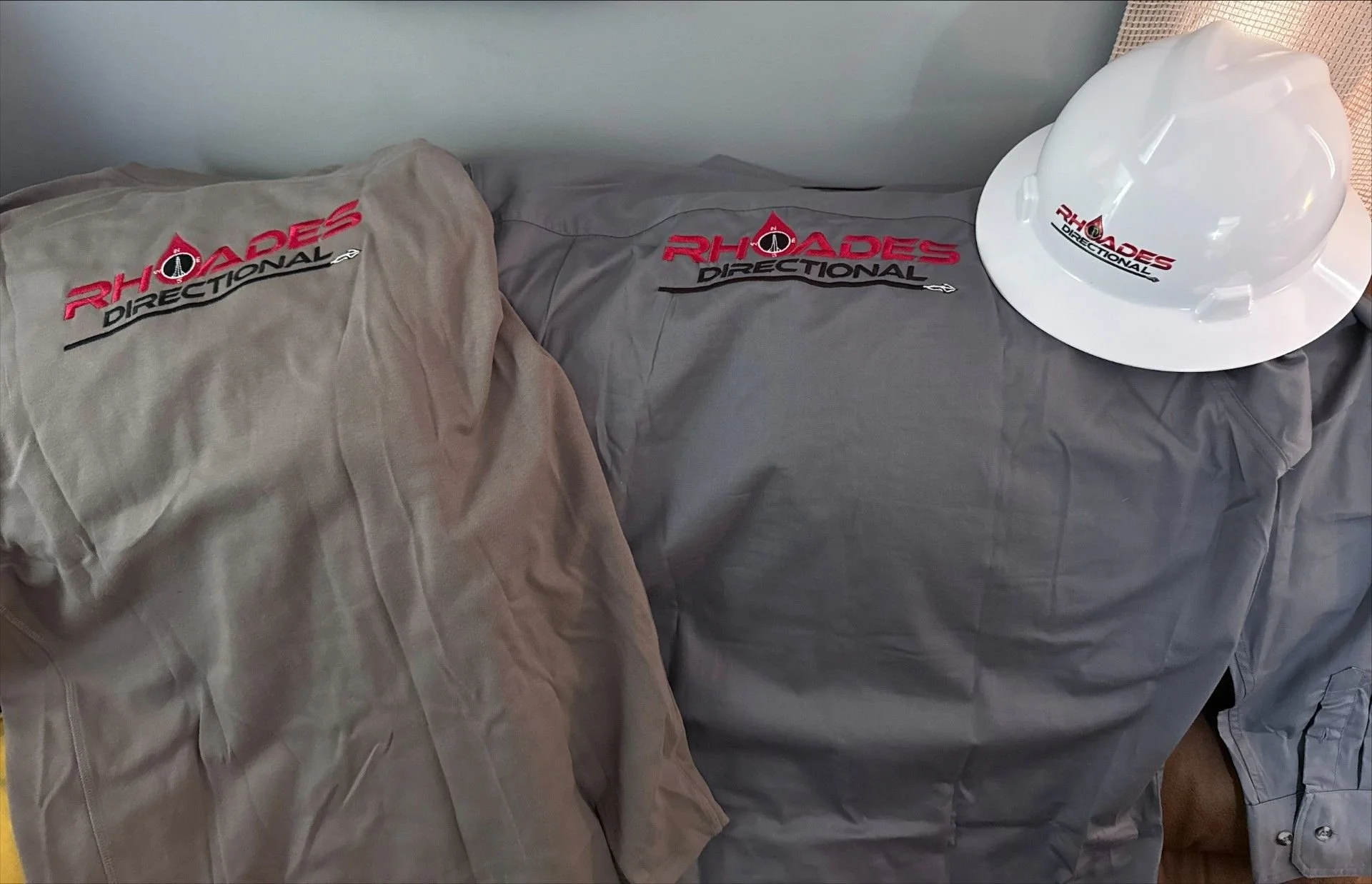 Two gray coveralls and a white construction helmet with the 'RHOADES DIRECTIONAL' logo embroidered or printed on them.