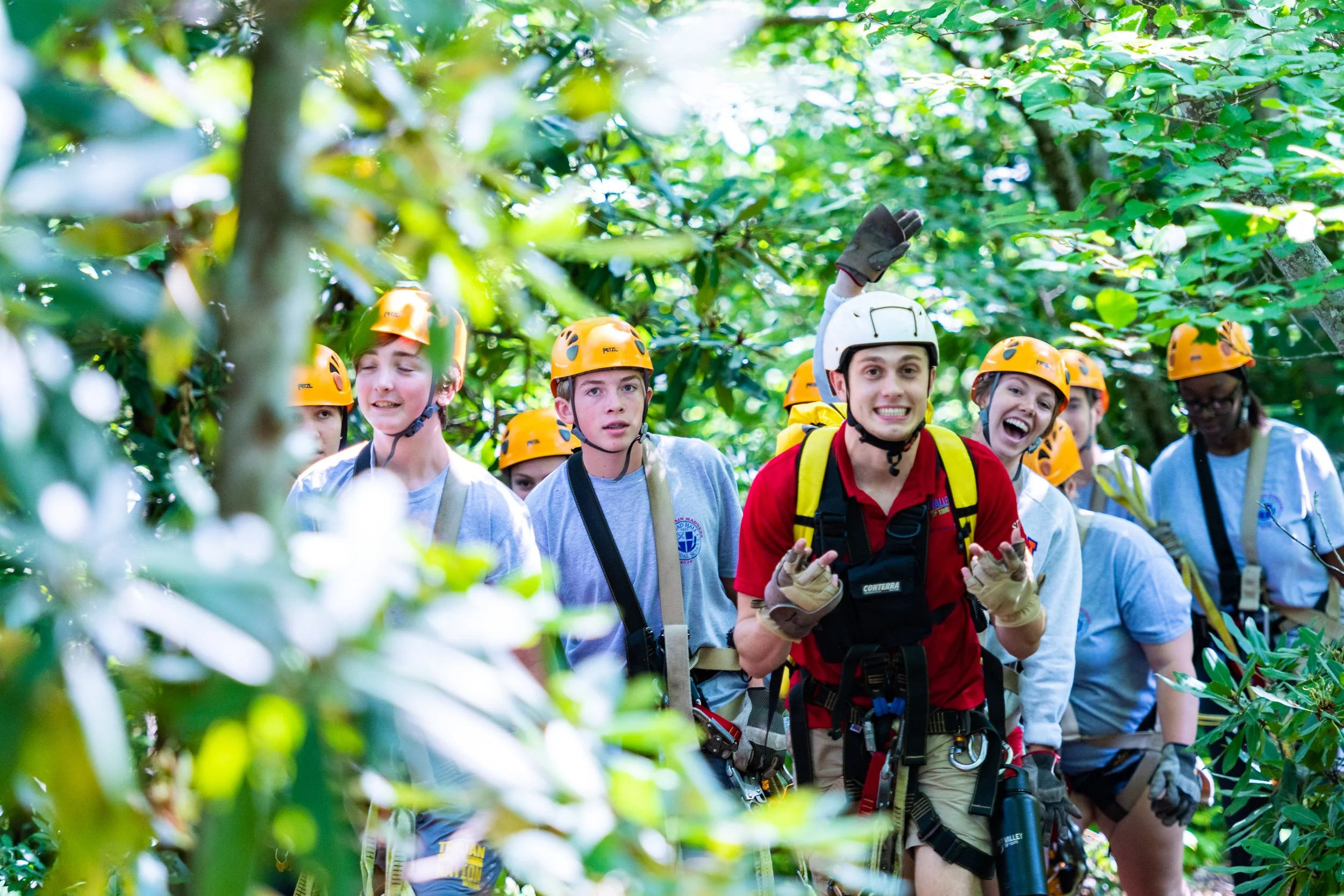 Group of people in a forest wearing helmets and safety gear, participating in a team-building or outdoor adventure activity.
