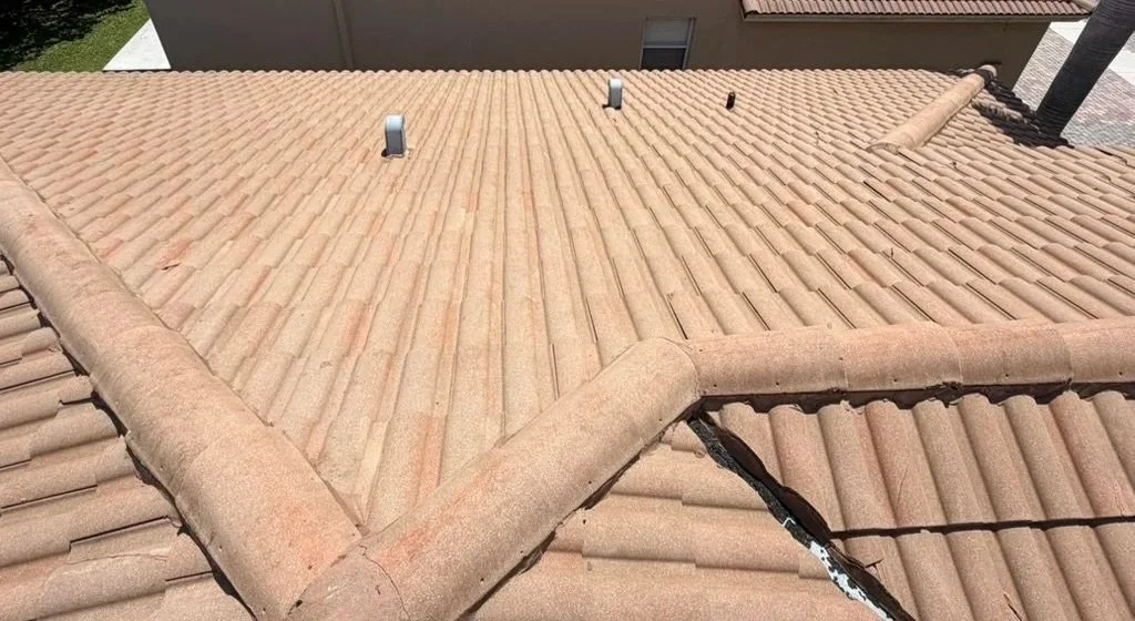 View of a tiled roof with a noticeable crack and some vents in sunlight.