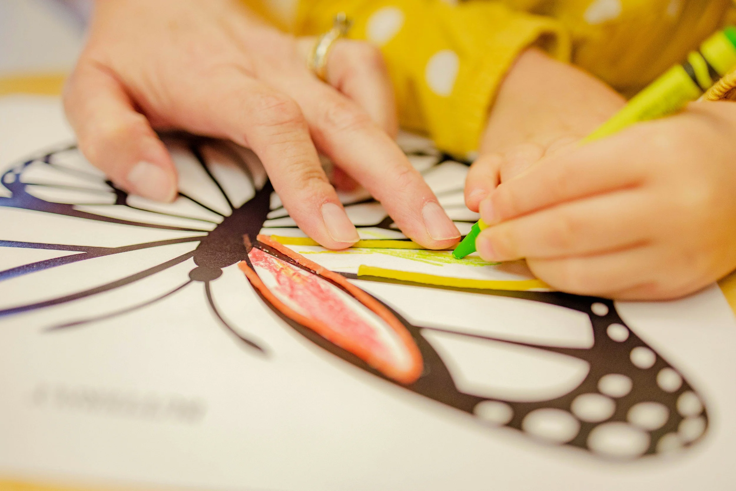 Close-up of hands coloring a printed image with crayons on paper.