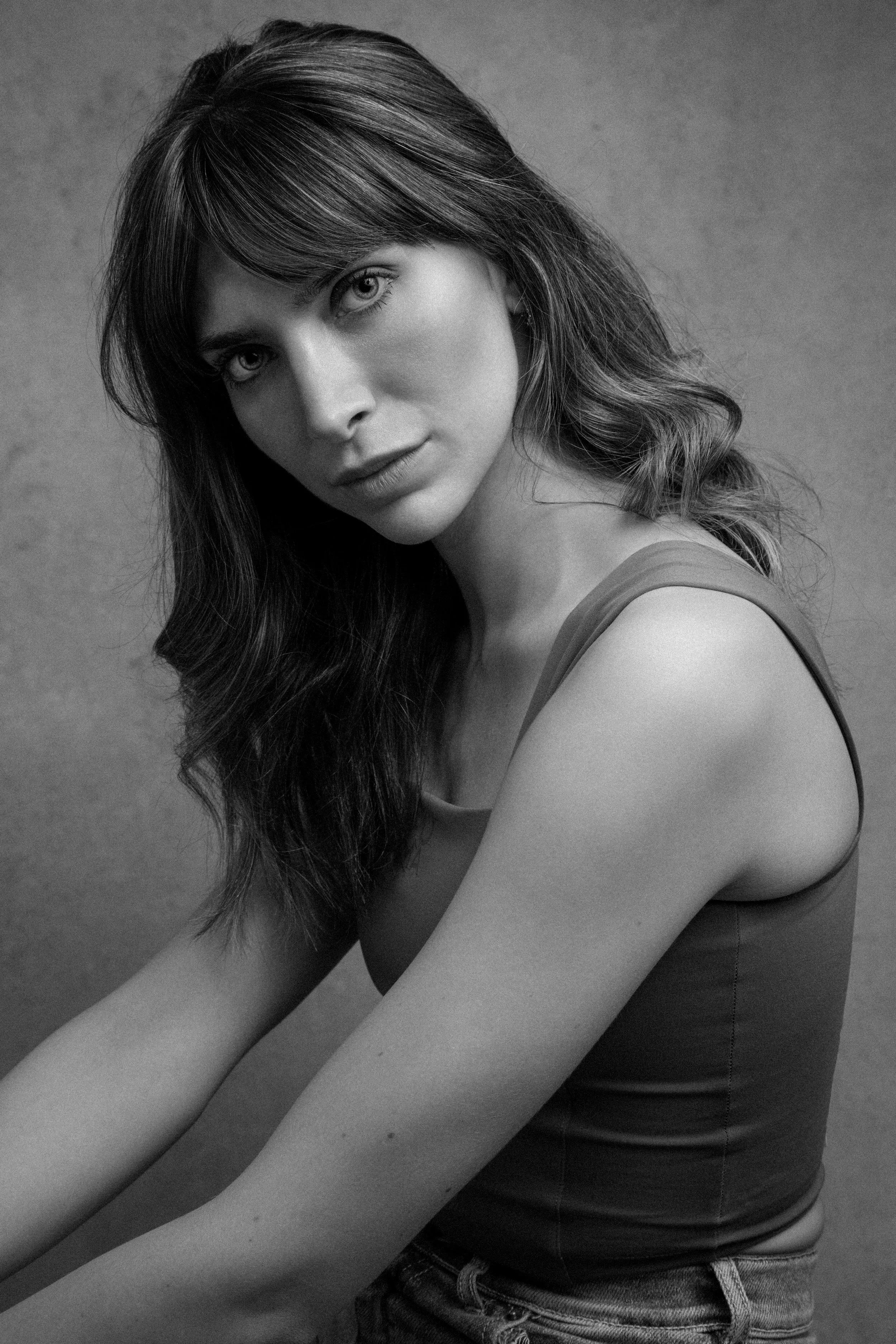 Black and white portrait of a woman with wavy hair, looking at camera, wearing a sleeveless top and jeans.