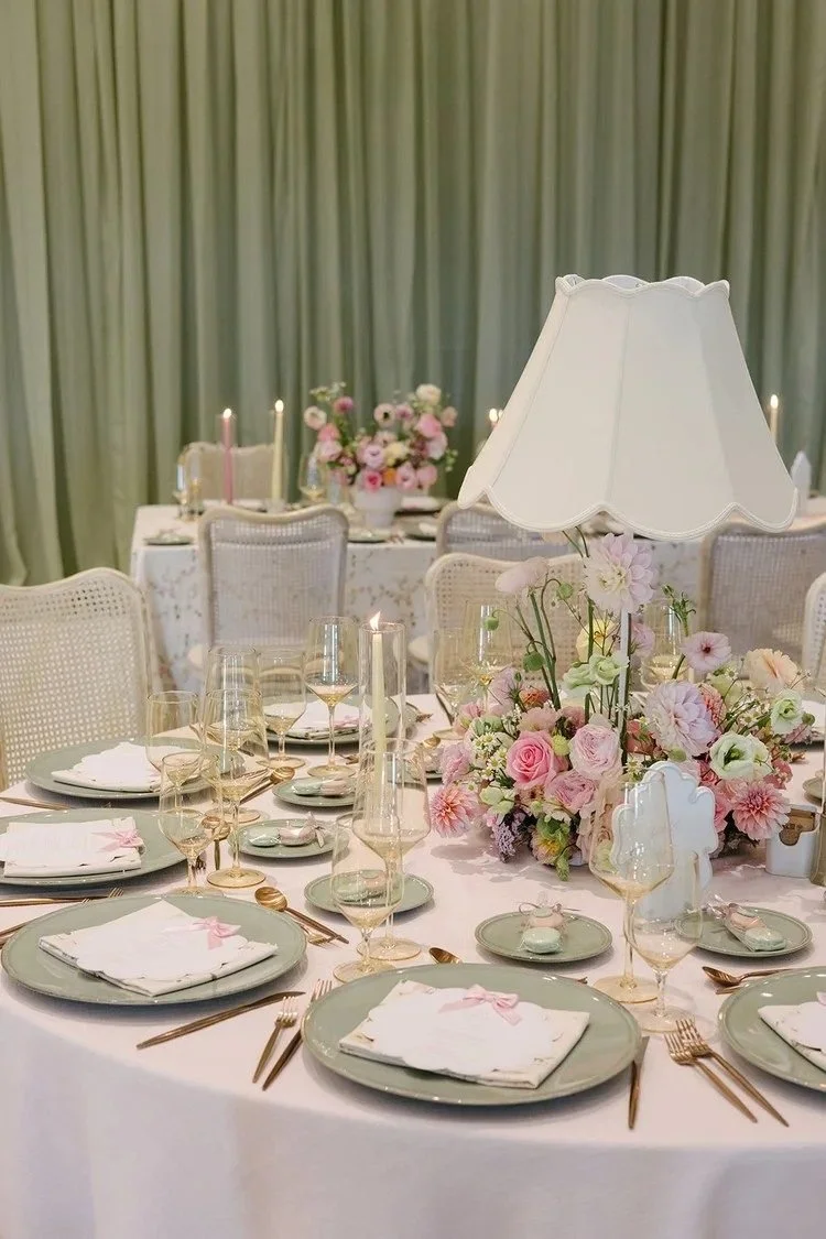 Elegant table set for a formal event with a large floral centerpiece, vintage-style chairs, and soft pastel colors.